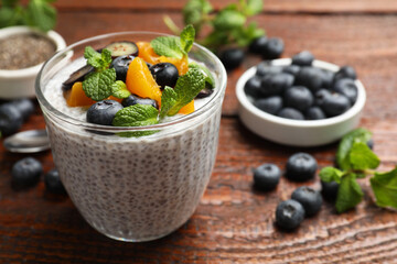 Delicious chia pudding with blueberries, peaches and mint in glass on wooden table, closeup
