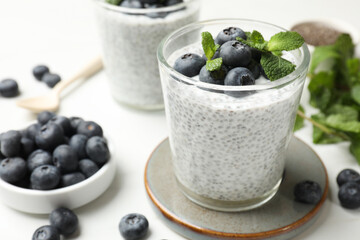 Delicious chia pudding with blueberries and mint in glasses on white table, closeup