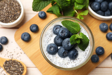 Delicious chia pudding with blueberries and mint in glass on wooden table, flat lay