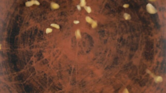 Bulgur groats are poured into a brown ceramic bowl. Top view. Slow motion.