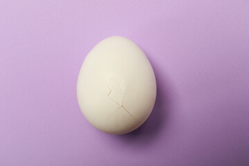 One egg with cracked shell on violet background, top view