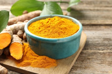 Turmeric powder in bowl, roots and leaves on wooden table, closeup