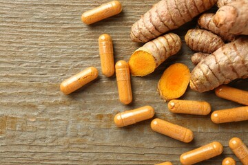 Turmeric capsules in spoon and roots on wooden table, flat lay. Space for text