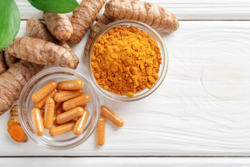 Turmeric capsules, powder, roots and leaves on white wooden table, flat lay. Space for text