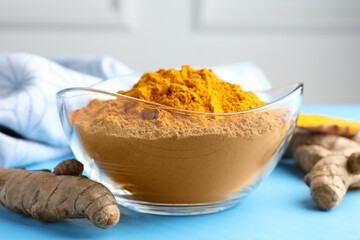 Aromatic turmeric powder in bowl and fresh roots on light blue wooden table, closeup