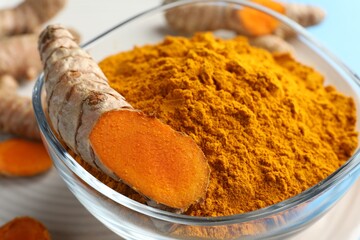 Aromatic turmeric powder in bowl and fresh roots on table, closeup