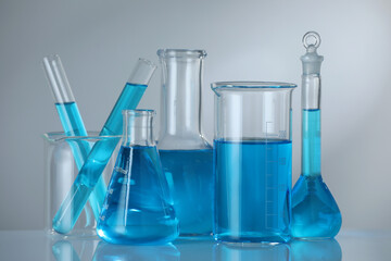 Laboratory glassware with blue liquid on mirror surface against grey background