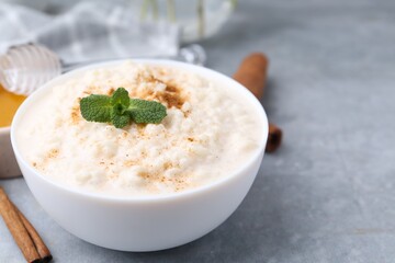 Tasty rice pudding with cinnamon and mint on light grey table, closeup. Space for text