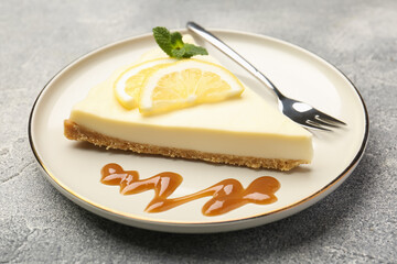 Piece of delicious lemon cheesecake with mint and caramel sauce on grey textured table, closeup