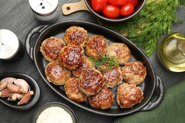 Delicious patties in baking dish, spices and tomatoes on black table, flat lay