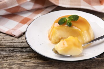 Delicious pudding with caramel sauce and mint served on wooden table, closeup