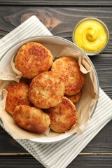 Tasty patties in bowl and mustard on wooden table, flat lay