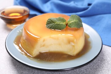 Delicious pudding with caramel sauce and mint on grey textured table, closeup