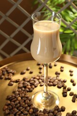 Coffee cream liqueur in glass and beans on tray, closeup