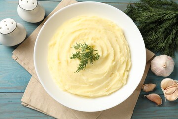 Tasty mashed potato with dill in bowl, garlic and spices on light blue wooden table, flat lay