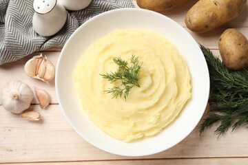 Tasty mashed potato with dill in bowl, raw vegetables and spices on light wooden table, flat lay