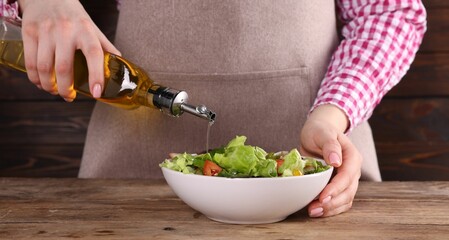 Woman pouring oil onto tasty salad at wooden table, closeup