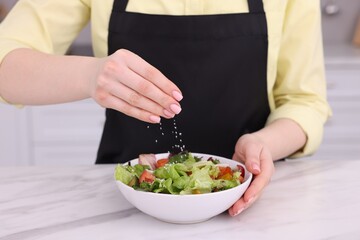 Woman salting tasty salad at white marble table indoors, closeup