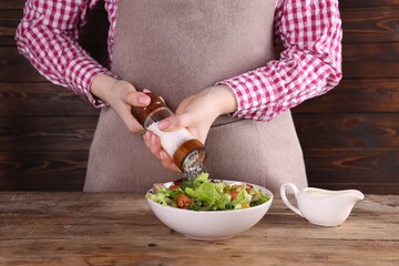 Woman salting tasty salad at wooden table, closeup