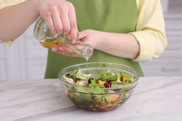 Woman pouring oil onto tasty salad at white marble table indoors, closeup