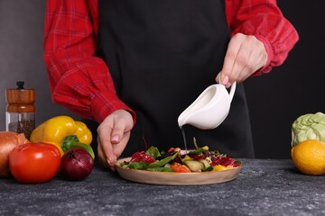 Woman pouring oil onto tasty salad at dark textured table, closeup