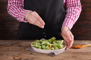 Woman salting tasty salad at wooden table, closeup