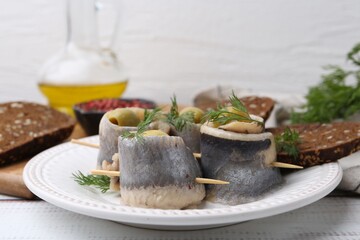 Delicious herring rolls with olives, dill and bread on white wooden table, closeup