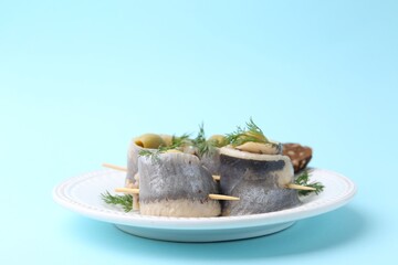 Delicious herring rolls with olives and dill on light blue background, closeup