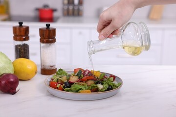 Woman pouring oil onto tasty salad at white marble table in kitchen, closeup