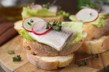Tasty sandwiches with herring, radish and lettuce on table, closeup