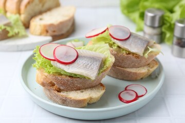Tasty sandwiches with herring, radish and lettuce on white tiled table, closeup