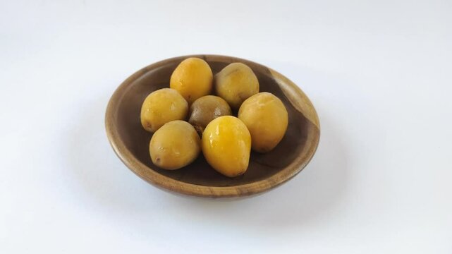 A group of fresh young dates or rutob dates or ruthob dates on a wooden plate with a white background.