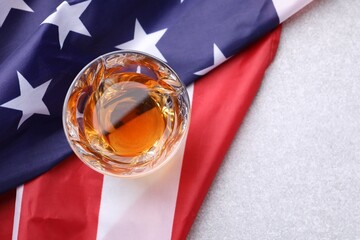 Glass of whiskey and American flag on light table, top view. Space for text