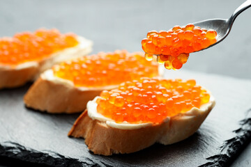 Putting tasty red caviar onto sandwiches on grey table, closeup