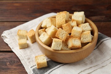Delicious crispy croutons in bowl on wooden table, closeup