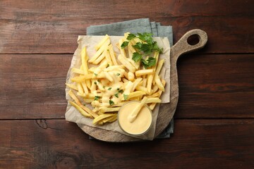 Delicious cheese sauce in bowl, French fries and parsley on wooden table, top view