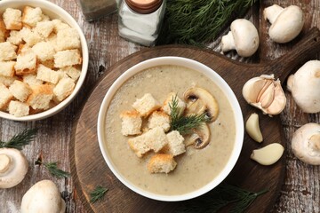 Delicious mushroom cream soup with croutons, dill and ingredients on wooden table, flat lay