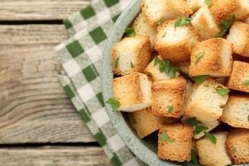 Tasty crispy croutons with cut parsley in bowl on wooden table, top view. Space for text