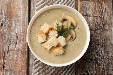Delicious mushroom cream soup with croutons and dill on wooden table, top view