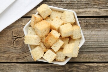 Tasty crispy croutons in bowl on wooden table, top view