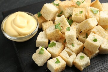 Tasty crispy croutons with cut parsley and sauce on dark table, closeup
