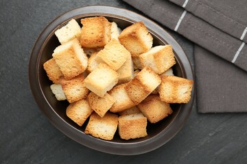 Tasty crispy croutons in bowl on dark textured table, top view