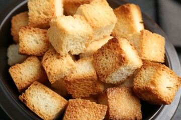 Tasty crispy croutons in bowl on table, closeup