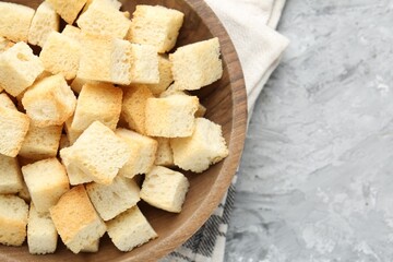 Tasty crispy croutons in bowl on grey textured table, top view. Space for text