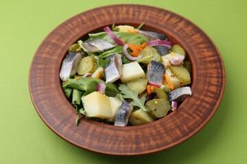 Delicious salad with herring, vegetables and mustard on green background, closeup