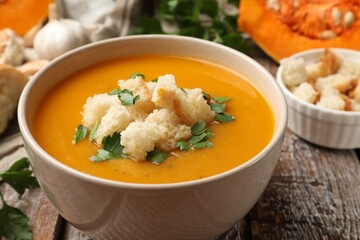 Tasty pumpkin cream soup with croutons and parsley in bowl on wooden table, closeup