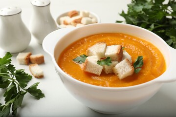 Tasty pumpkin cream soup with croutons and parsley in bowl on white table, closeup
