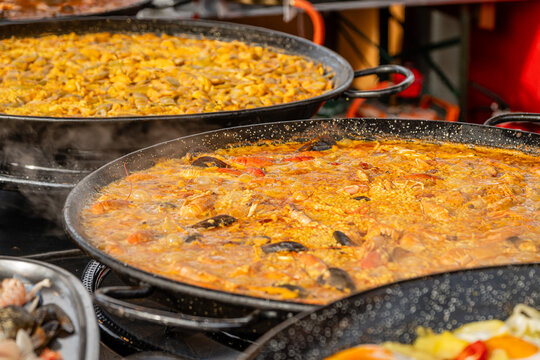 Large pans of delicious spanish paella are cooking at an outdoor food market, steaming hot and ready to eat