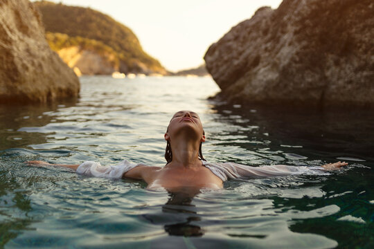 Nude sexy woman in water at sunset. Beautiful blonde woman with short wet hair and big breasts, art portrait in sea