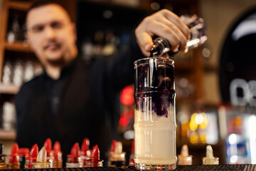 Close up of bartender adding liquor into glass and making cocktail in a bar.